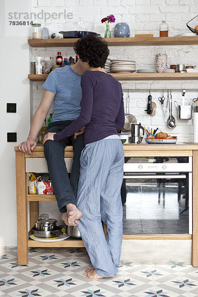 Ein altersgemischtes Paar  das sich in seiner Küche küsst.