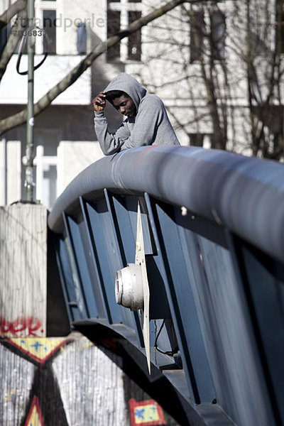 Ein hipper junger Mann  der auf einer Brücke steht und nach unten schaut.