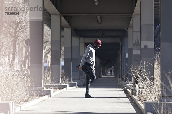 Ein junger Mann  der sich auf einem Bürgersteig unter einer Stadtbrücke ausstreckt.