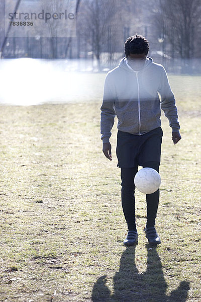 Ein junger Mann tritt einen Fußball in einem Stadtpark.