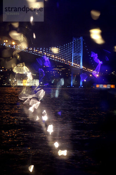 Reflektiertes Licht und Blick auf eine beleuchtete Brücke über Wasser bei Nacht