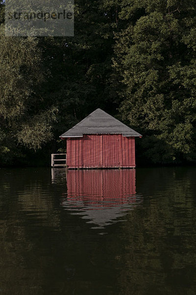 Ein rotes Bootshaus inmitten von Bäumen an einem See