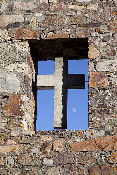 Ein Kreuz in einem offenen Fenster der Steinmauer einer Kirche