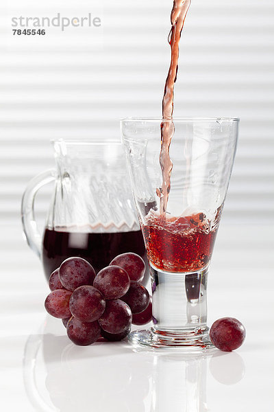 Karaffe und Glas mit gießendem roten Traubensaft  Nahaufnahme