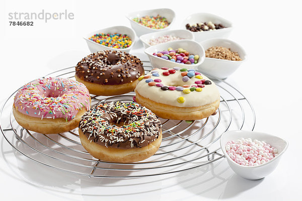 Variety of doughnuts on cooling rack besides bowl of sprinkles