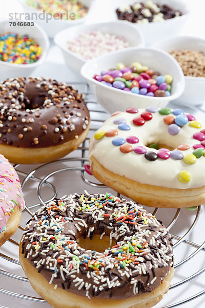 Variety of doughnuts on cooling rack besides bowl of sprinkles