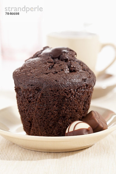 Plate of chocolate muffin with praline  coffee cup in background