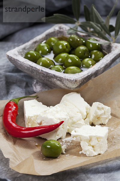 Schale mit grünen Oliven in Olivenöl mit Schafskäse und Chili auf Textil  Nahaufnahme