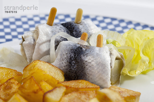 Rollmop herring with roasted potatoes and onions on a plate
