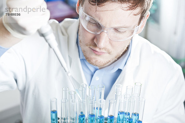 Deutschland  Junge Wissenschaftlerin pipettiert blaue Flüssigkeit in Reagenzgläser  Nahaufnahme