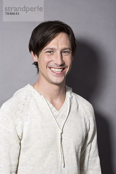 Porträt eines jungen Mannes vor grauem Hintergrund  lächelnd
