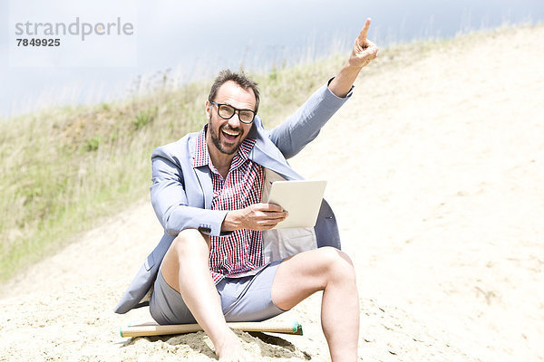 Deutschland  Bayern  Portrait eines Geschäftsmannes auf Sand sitzend mit digitaler Tafel  lächelnd