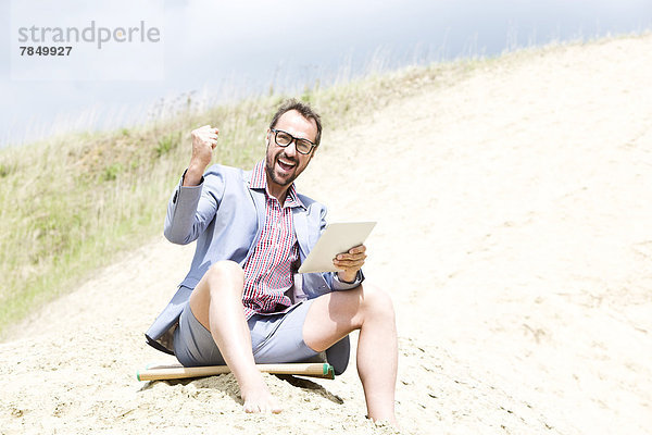 Deutschland  Bayern  Portrait eines Geschäftsmannes auf Sand sitzend mit digitaler Tafel  lächelnd