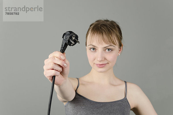 Porträt einer jungen Frau mit Netzstecker vor grauem Hintergrund