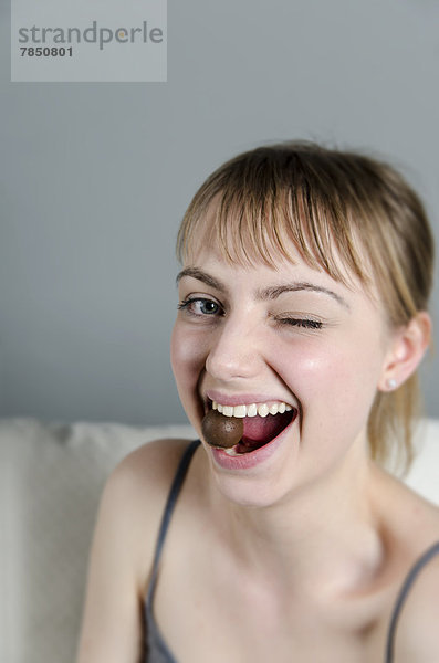 Porträt einer jungen Frau  die Schokoladenpraline isst  lächelnd