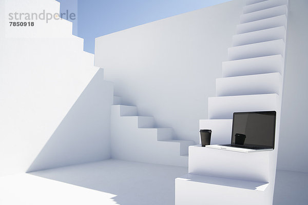 Laptop mit Einwegbecher auf weißer moderner Treppe