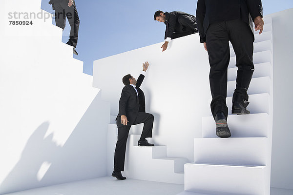 Geschäftsleute  die Treppen steigen  nach unten gehen und einem anderen Mann beim Aufstieg helfen.