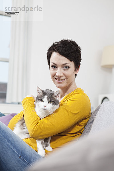 Porträt einer mittleren erwachsenen Frau mit Katze auf der Couch  lächelnd