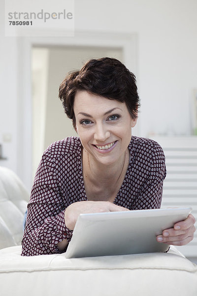 Porträt einer mittleren erwachsenen Frau mit digitalem Tablett auf der Couch  lächelnd