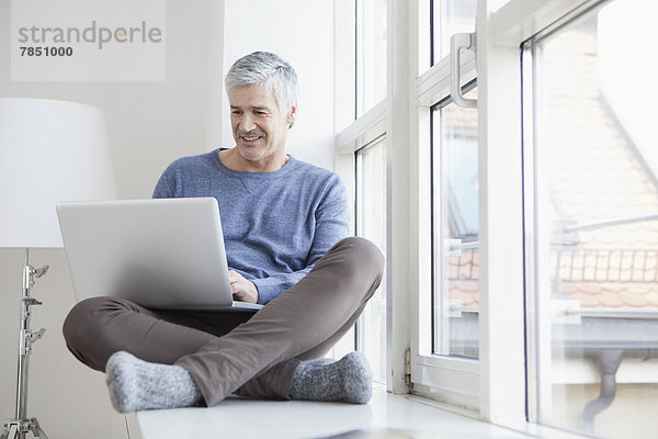 Erwachsener Mann am Fenster sitzend und mit Laptop