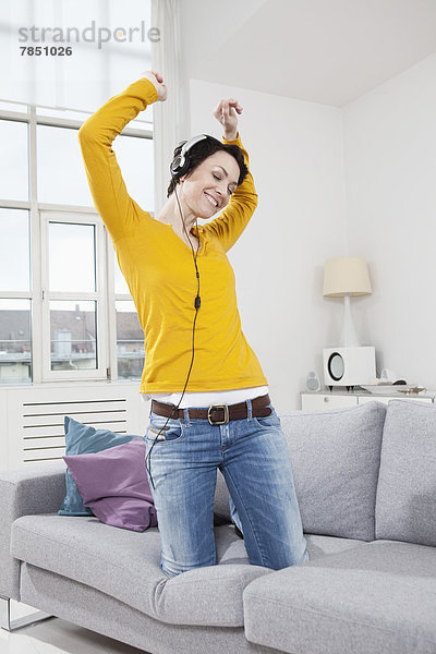 Mittlere erwachsene Frau  die Musik auf der Couch hört  lächelnd