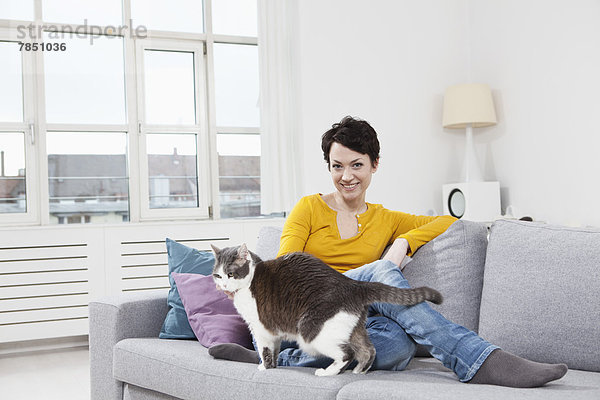 Porträt einer mittleren erwachsenen Frau mit Katze auf der Couch  lächelnd