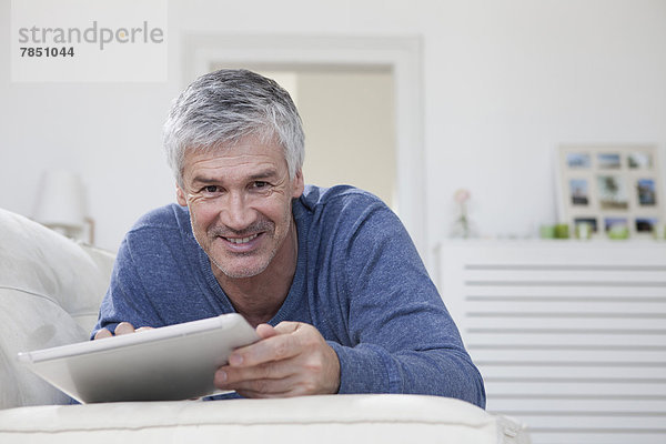 Porträt eines reifen Mannes mit digitalem Tablett auf der Couch  lächelnd