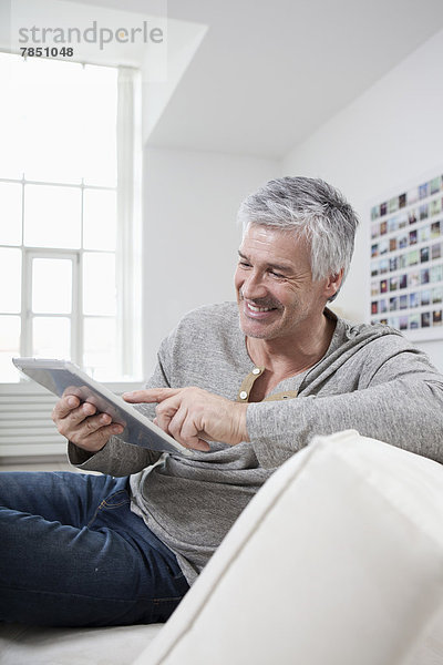 Erwachsener Mann mit digitalem Tablett auf der Couch  lächelnd