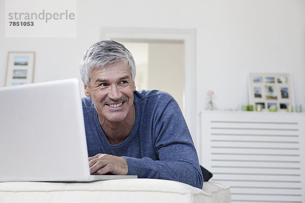 Erwachsener Mann mit Laptop auf der Couch  lächelnd