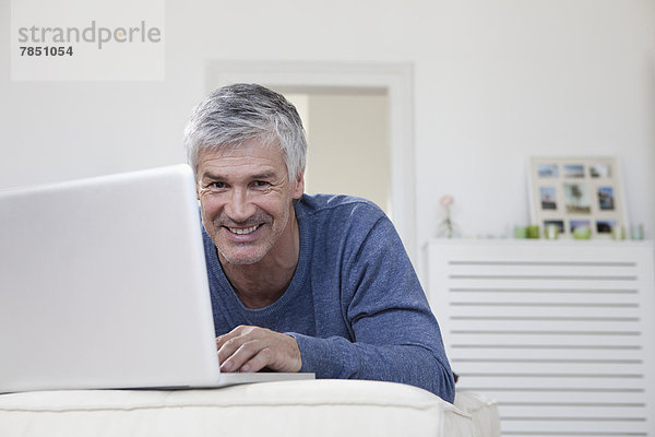 Portrait eines reifen Mannes mit Laptop auf der Couch  lächelnd
