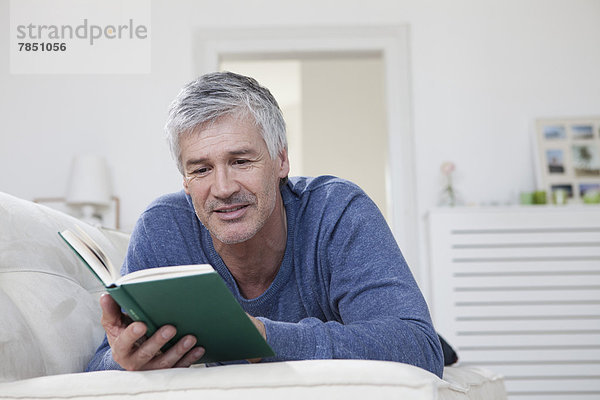 Erwachsener Mann liest Buch auf der Couch  lächelnd
