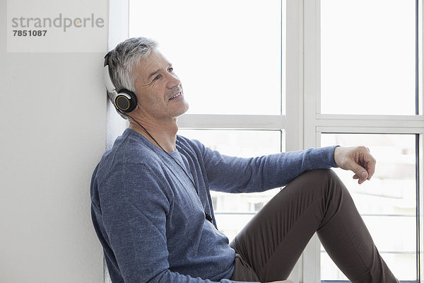 Erwachsener Mann am Fenster sitzend mit Musik  lächelnd