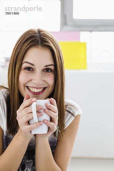 Porträt einer jungen Frau  die eine Tasse hält  lächelnd