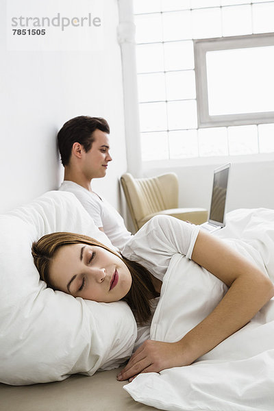 Junge Frau schläft  während junger Mann Laptop im Hintergrund benutzt