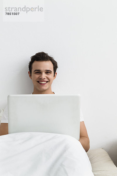 Portrait eines jungen Mannes mit Laptop  lächelnd