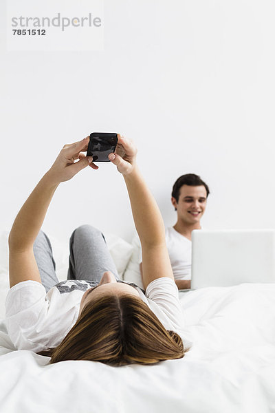 Junge Frau mit Handy  junger Mann mit Laptop im Hintergrund  lächelnd