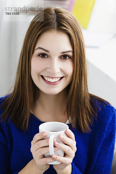 Porträt einer jungen Frau  die eine Tasse hält  lächelnd