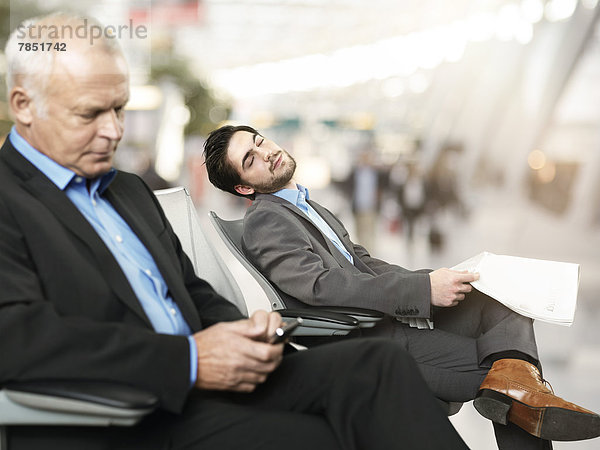 Älterer Mann  der das Handy benutzt  während der mittlere erwachsene Mann im Hintergrund schläft.