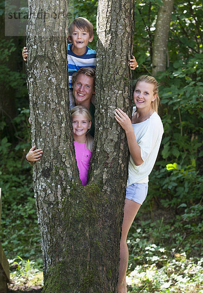 Österreich  Portrait von Freunden  die hinter einem Baumstamm stehen  lächelnd