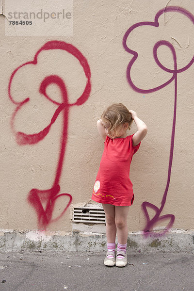 Kleines Mädchen an der Wand lehnend mit Blumengraffiti  Portrait
