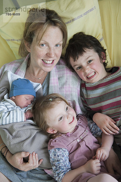 Mutter auf Krankenhausbett sitzend mit Kindern und Neugeborenen  Portrait