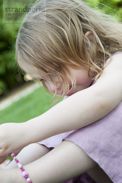Kleines Mädchen im Freien sitzend  mit Perlenkette spielend