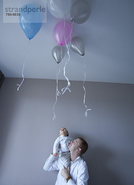 Vater trägt Baby auf der Schulter  Baby blickt auf schwebende Luftballons