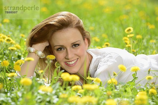 Junge Frau liegt auf einer Löwenzahn-Wiese im Frühling  Portrait