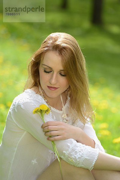 Junge Frau sitzt auf einer Löwenzahn-Wiese im Frühling