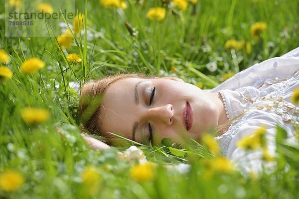 Junge Frau liegt auf einer Löwenzahn-Wiese im Frühling  Portrait