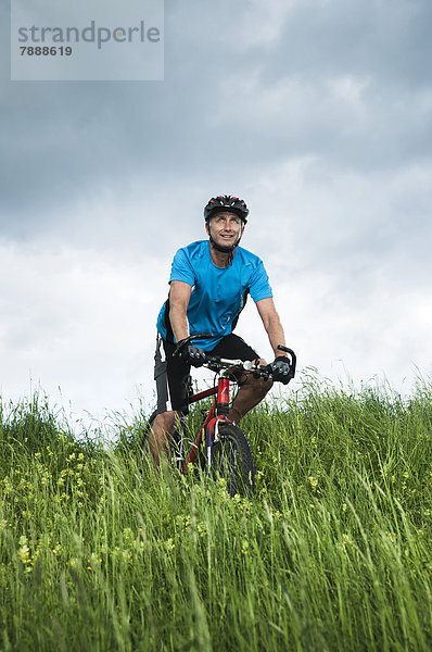 Reifer Mann mit Mountainbike auf einem Feld