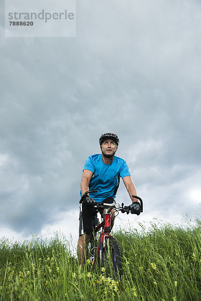 Reifer Mann mit Mountainbike auf einem Feld
