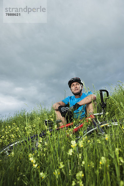 Reifer Mann mit Mountainbike sitzt auf einem Feld