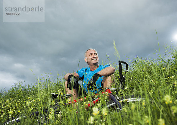 Reifer Mann mit Mountainbike sitzt auf einem Feld